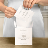 Person holding Tavalon tea packages with a white tea box on a wooden surface.