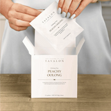 Tavalon Peachy Oolong tea packaging with a hand opening it on a wooden surface.