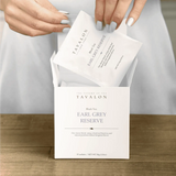 Tavalon Earl Grey Reserve tea packaging with tea bags being removed on a wooden surface.