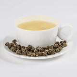 Jasmine Pearls tea in a white teacup with loose leaf tea in a saucer