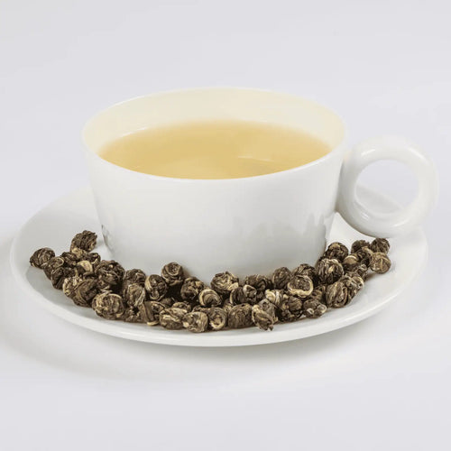 Jasmine Pearls tea in a white teacup with loose leaf tea in a saucer