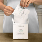 Person opening a Tavalon Jasmine Pearls green tea box on a wooden surface.