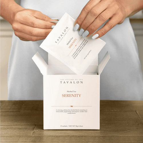 Tavalon Serenity herbal tea packaging with hands opening it on a wooden surface.